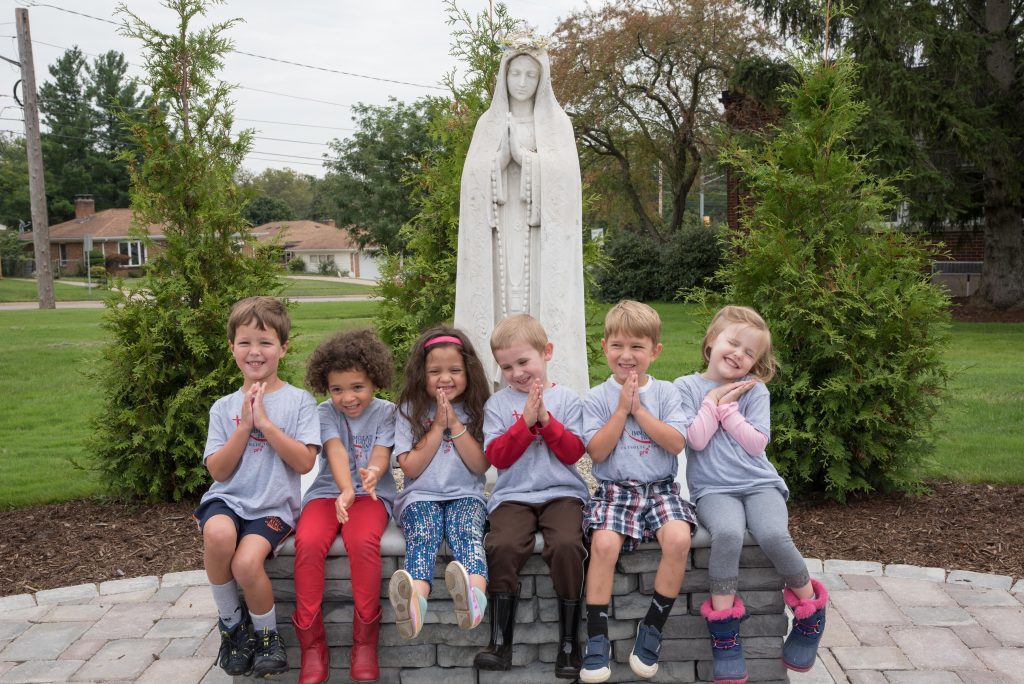 young students with prayer hands in front of Mary statue